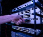 A close-up of a person's hand unplugging a network cable from a server rack, surrounded by glowing indicator lights in a dimly lit environment.