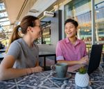 Students sitting at a table outside, smiling and with a laptop. 