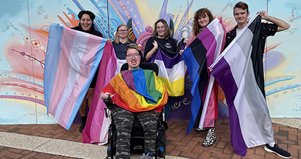 a group of students standing with the pride flag
