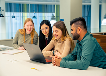 Four students are gathered around a laptop at a desk 