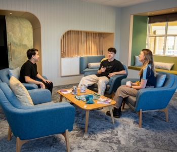 Three students sitting in a relaxed lounge space in The Living Room Joondalup, chatting together on blue armchairs around a coffee table.